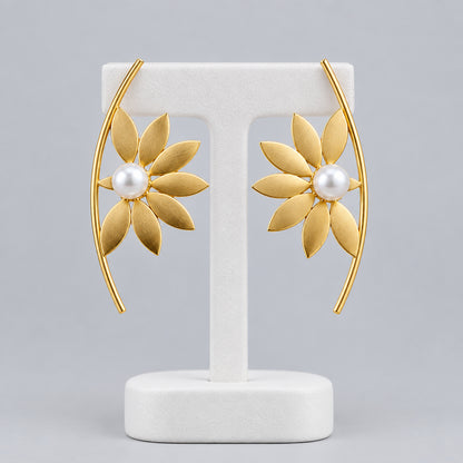 A pair of gold crescent-shaped brass earrings with a central white pearl and radiating petal details.