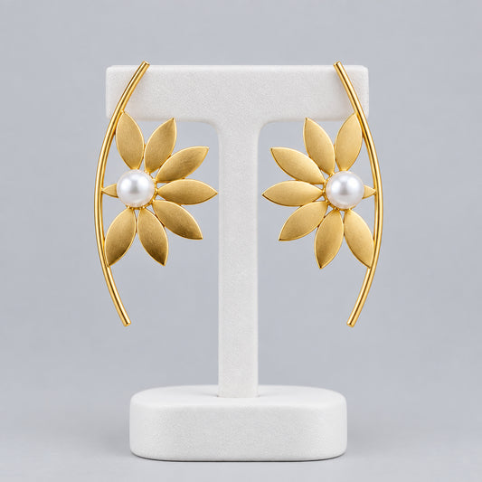 A pair of gold crescent-shaped brass earrings with a central white pearl and radiating petal details.