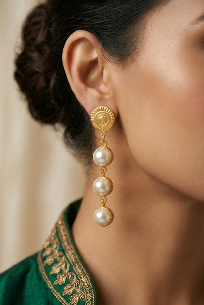 A pair of gold-plated drop earrings with three white faux pearls hanging from textured gold circular studs, made in brass.