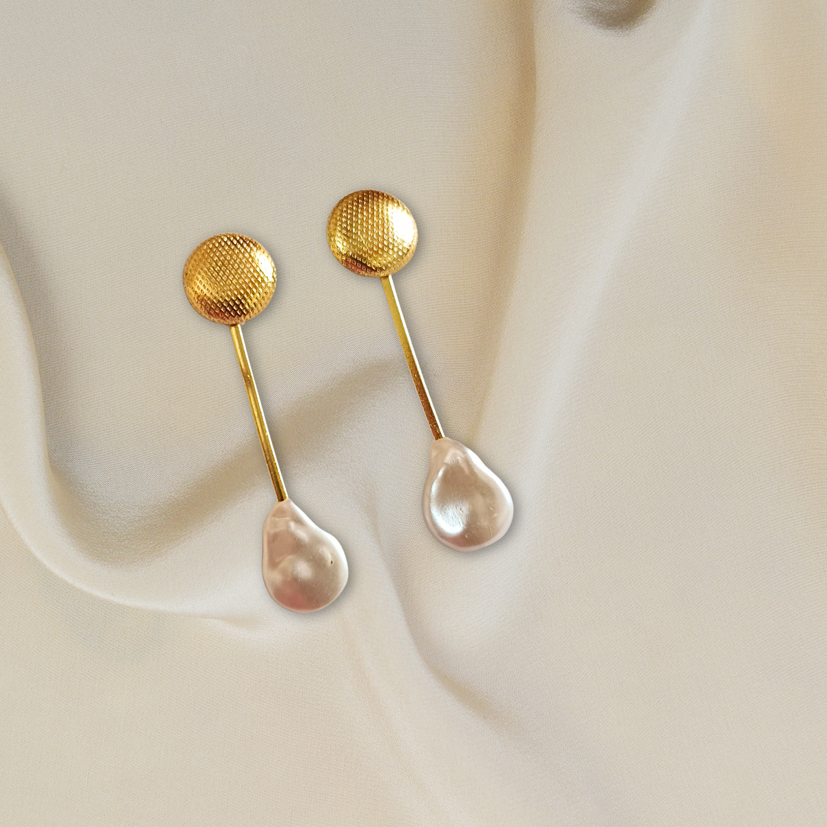 A pair of gold-toned brass stud earrings with textured circular tops, slim bars, and teardrop-shaped mother of pearls.