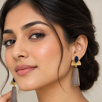 A pair of gold-toned statement brass earrings with dark blue teardrop-shaped stones and large rectangular taupe-gray stone